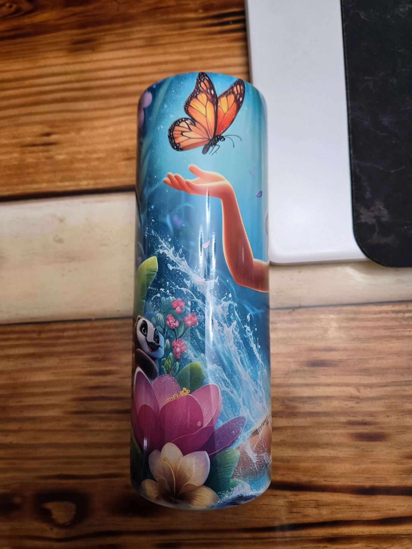 Moana tumbler cup featuring a character reaching for a butterfly amidst vibrant flowers and water, perfect for fans.