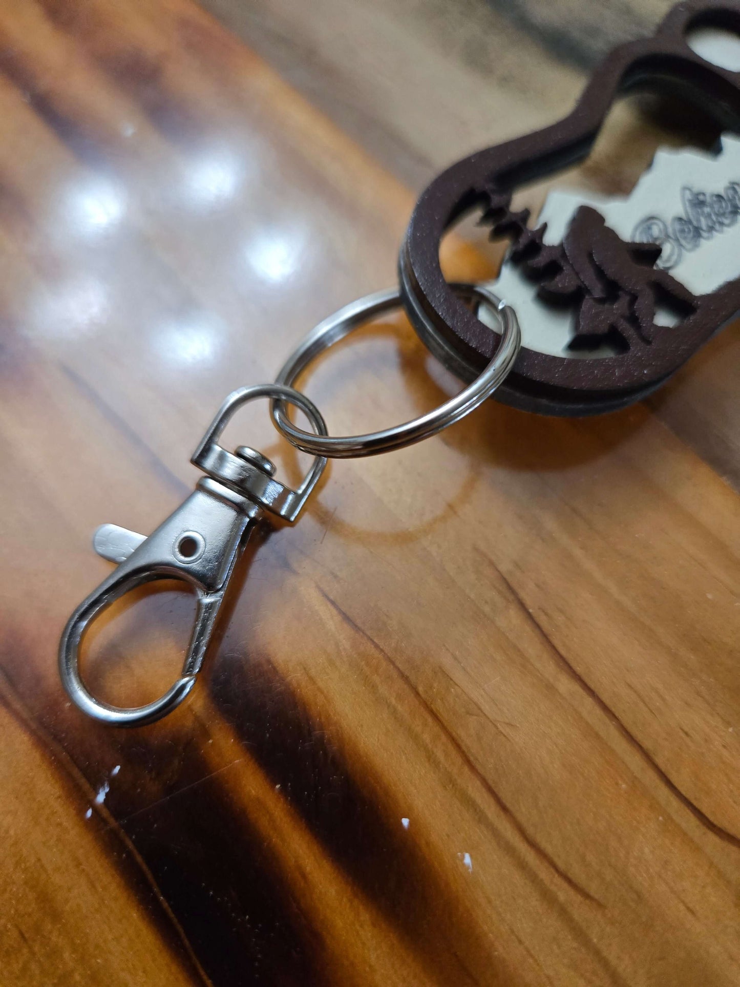 Close-up of Bigfoot keychain with metal clasp on wooden surface, perfect for travel and organization.