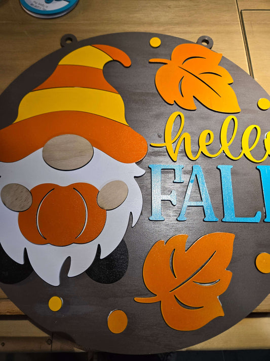 Decorative sign with autumn-themed elements including leaves, a pumpkin, and a candy corn on a dark background.