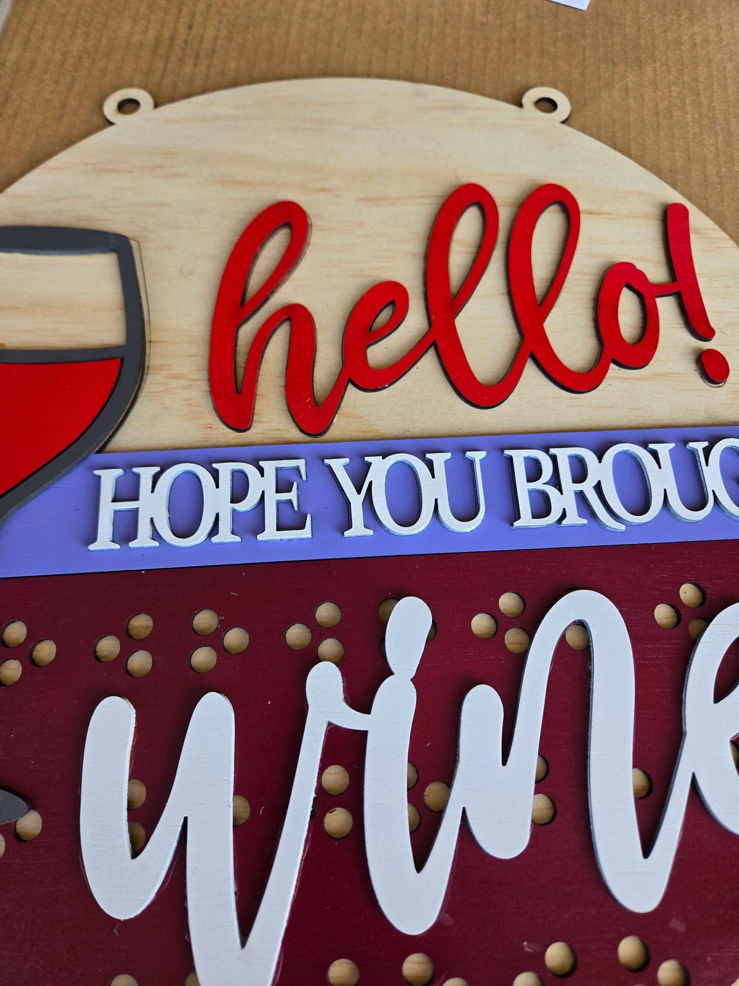 Close-up of a wooden sign featuring the phrase 'Hope You Brought Wine' with a wine glass design.
