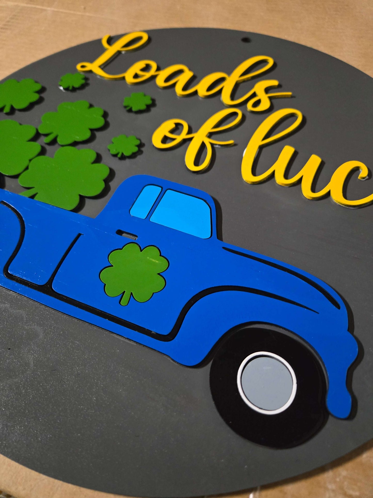 St. Patrick's Day wooden sign featuring a blue truck and the phrase 'Loads of Luck' with shamrocks.