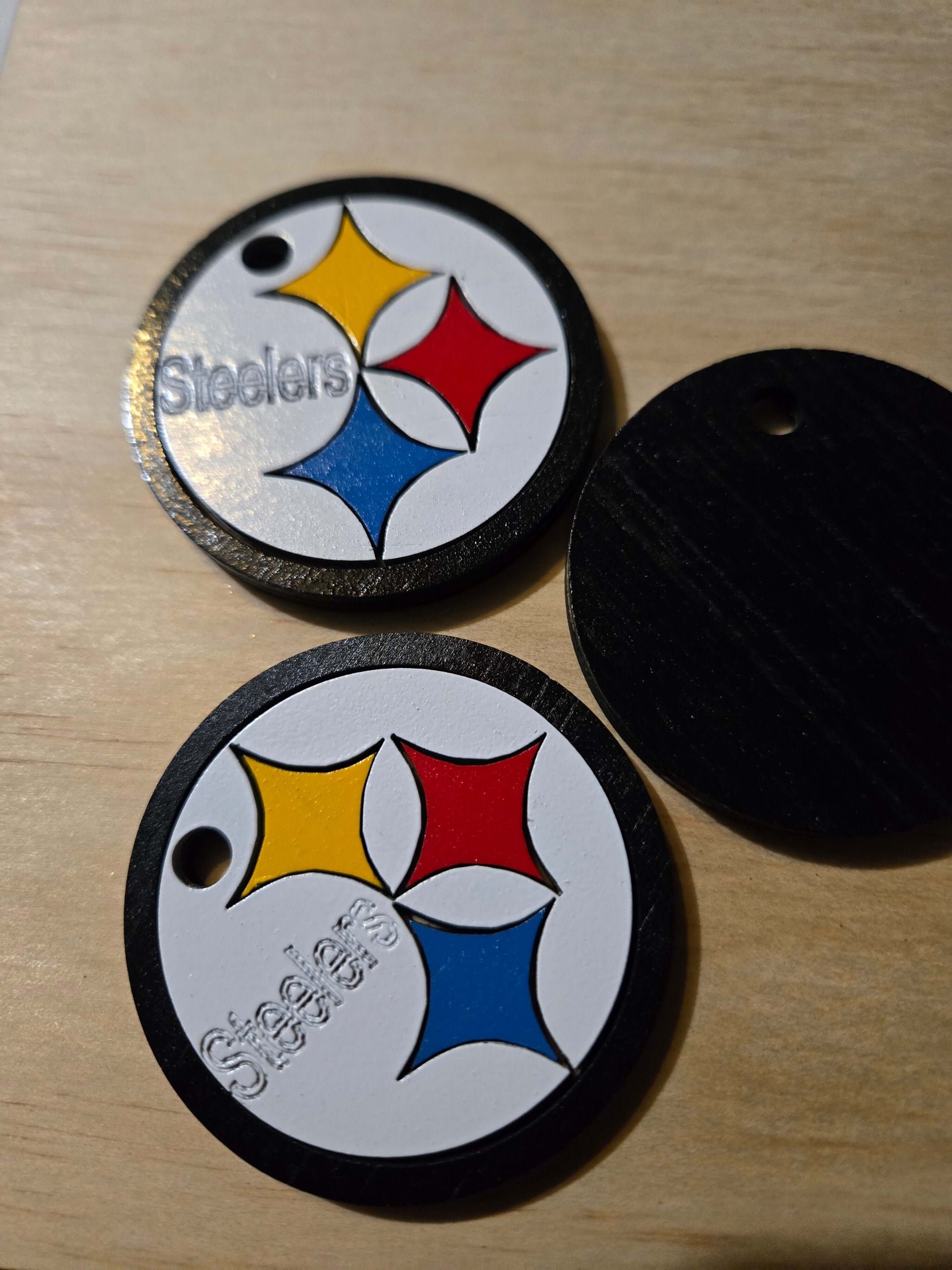 Pittsburgh Steelers logo keychains in vibrant colors on a wooden surface.