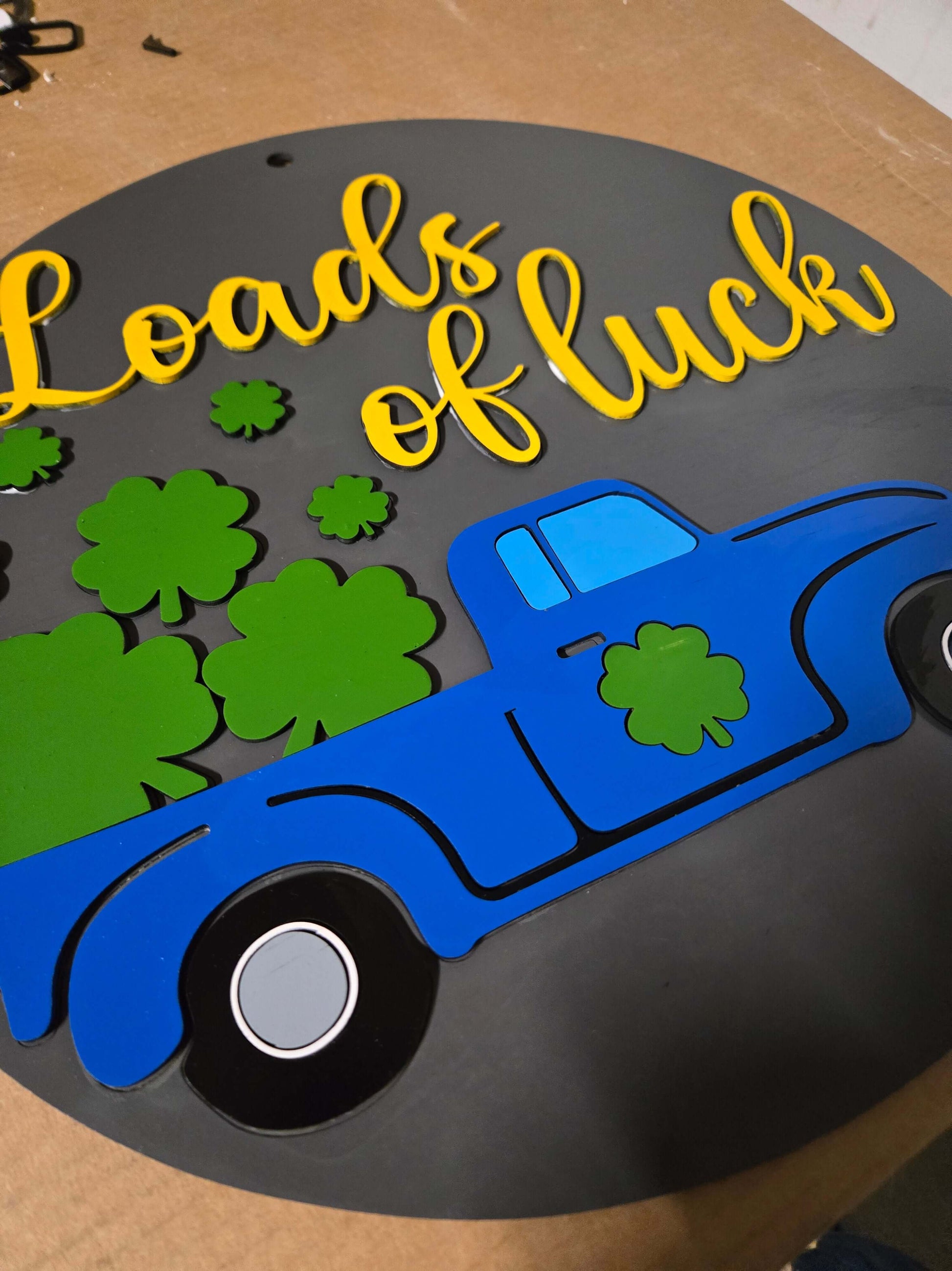 St. Patrick's Day wooden decor sign with blue truck and green shamrocks that reads 'Loads of luck'.
