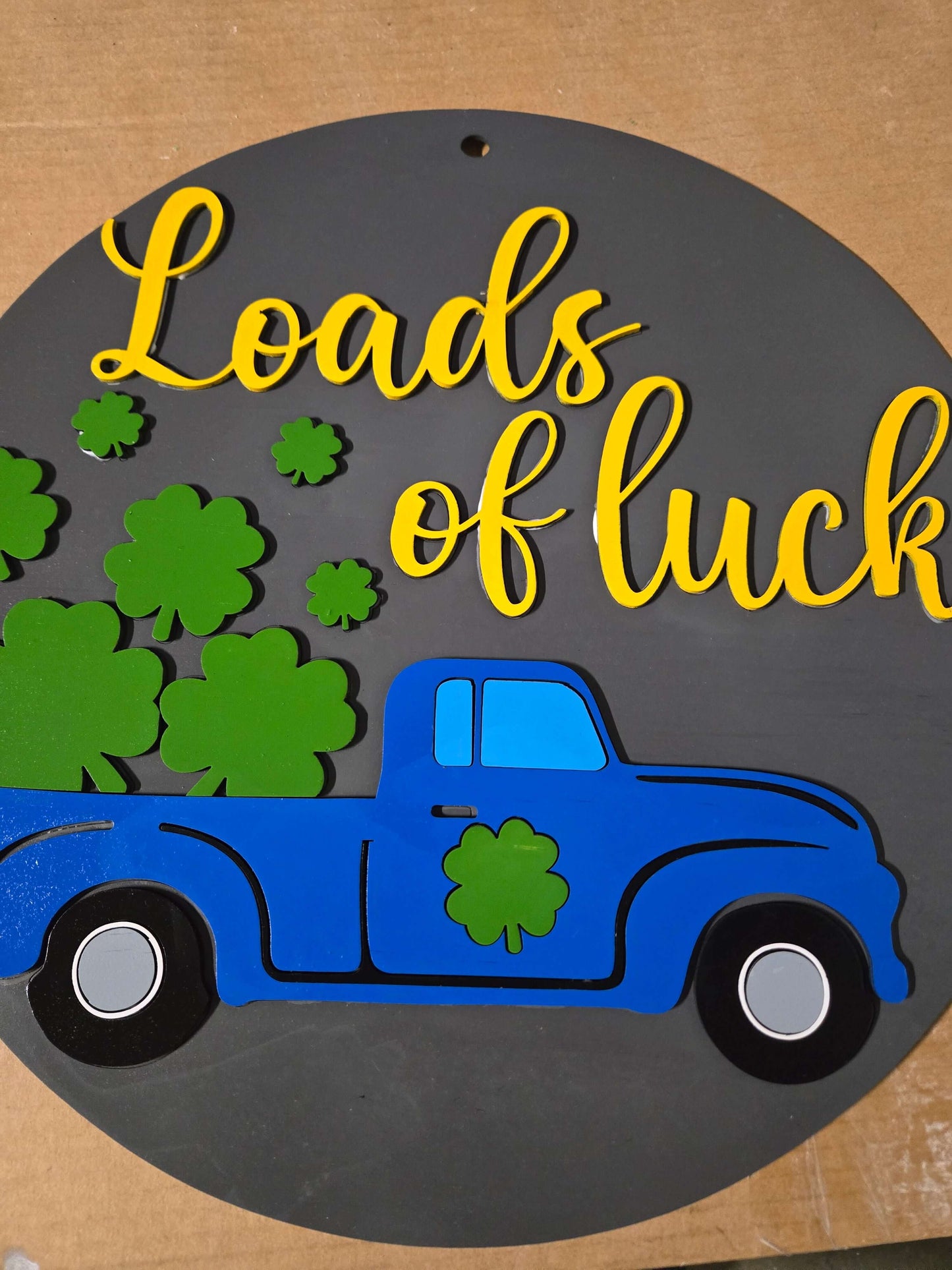 St. Patrick's Day wooden decor sign with blue truck, green clovers, and whimsical lettering 'Loads of luck'.